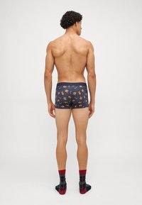 Marinblå boxershorts med en färgglad mönstring av godiskäppar och lejon; mjukt tyg med elastisk midja, kombinerat med rutig strumpor.