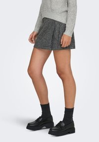 Pull en maille gris, jupe plissée noire et mocassins noirs épais avec chaussettes texturées, présentant une finition lisse et un motif côtelé.