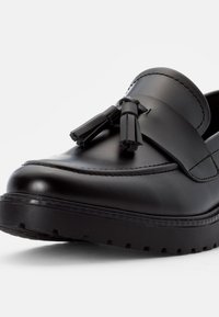 Mocassins en cuir noir avec une finition lisse, dotés d'un détail décoratif en gland et d'une semelle en caoutchouc épaisse. Bout arrondi et accents cousus.