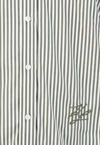 Hvit og olivengrønn vertikalt stripet skjorte med hvite knapper og en brodert monogram på nederste høyre side.