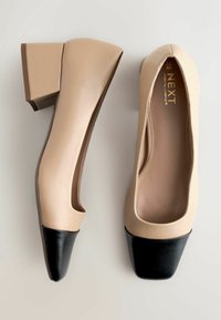 Pantof bej din piele, cu vârful pătrat, având o închidere din piele neagră și un toc bloc. Textură netedă cu un design minimal.