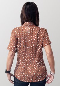 Camicia marrone a maniche corte con pois bianchi, dotata di colletto e dettaglio plissettato sul retro. Tessuto strutturato, vestibilità casual.