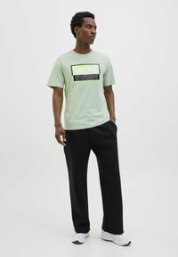 Lys grøn t-shirt med sort og gul grafisk tekst, parret med sorte, løstsiddende bukser og hvide sportsko.