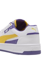 Hvide sneakers med gule og lilla accenter, lædermateriale, polstret krave, rund tå og en struktureret sål med PUMA-logoet.