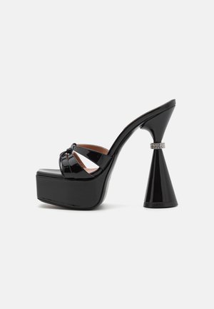 Zapato de tacón alto de plataforma negro de charol con tacón cónico, que presenta correas entrelazadas y un acento metálico cerca del tacón.