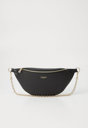 Sac à main en cuir synthétique noir avec une forme incurvée, une bandoulière en chaîne dorée et une fermeture éclair. Présente le logo Lacoste à l'avant.