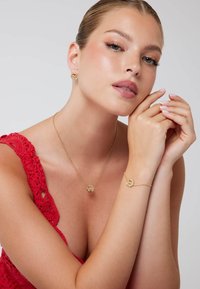 Set di gioielli in oro composto da una collana e un bracciale con pendenti circolari, abbinati a orecchini a stud. Il modello indossa un top rosso all'uncinetto.