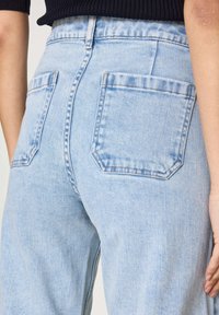 Jeans in denim blu chiaro con due tasche posteriori a forma quadrata e dettagli cuciti. Il materiale ha una finitura morbida e testurizzata.