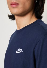 Jūras zilas krāsas ikdienas t-krekls ar apaļu dekoltē, izgatavots no mīkstas auduma, ar mazu baltu izšūtu Nike logotipu uz krūšu daļas. Gluda tekstūra, vienkāršs dizains.