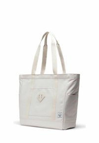 Sac fourre-tout en toile beige avec deux longues poignées, poche avant, poches latérales, patch en forme de losange et petite étiquette de marque près du coin inférieur.