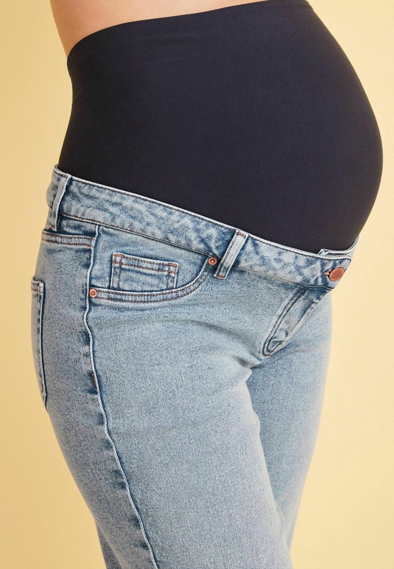 I jeans premaman azzurro chiaro presentano un design aderente con un alto pannello elastico nero e accenti di cucitura sottili.
