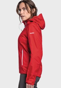 Red jacket with a hood, made of smooth, weather-resistant material. Features white zippers and a fitted design with adjustable cuffs.