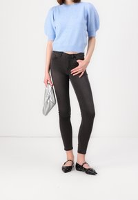 Ljusblå kort tröja med puffärmar, kombinerad med mörka smala jeans, svarta ballerinaskor med hålmönster och en silverfärgad kuvertväska.