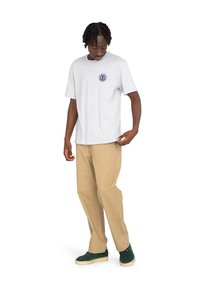 Graues Baumwoll-T-Shirt mit kurzen Ärmeln und einem kreisförmigen navyblauen Grafikdesign auf der Brust, kombiniert mit beigen Hosen und grünen Turnschuhen.