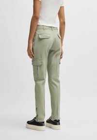 Ljusgröna cargobyxor med sidofickor och dragkedjeärmar, tillverkade av mjukt tyg. Matchat med svarta sneakers med tjock vit sula.