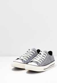 Baskets en toile à carreaux noir et blanc avec lacets blancs, embouts en caoutchouc et une bande noire sur la semelle. Design classique à coupe basse.