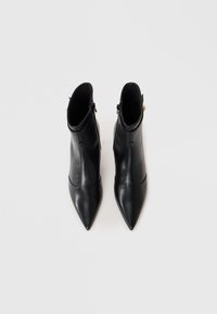 Bottines en cuir noir avec un bout pointu, texture lisse et zips latéraux. Présente un design courbé et de subtils détails de couture.