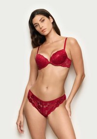 Röd spets-bh med vadderade kupor och scallopkanter samt justerbara band. Matchande spets-trosa med blommönster och elastiskt midjeband.