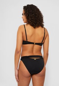 Svart bikini-sett med halterneck topp med justerbare stropper og klassiske truser med vridd detalj og gull akcent.