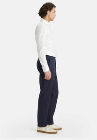 White long-sleeve shirt paired with navy trousers and light sneakers. The outfit features a fitted design and a smooth texture.
