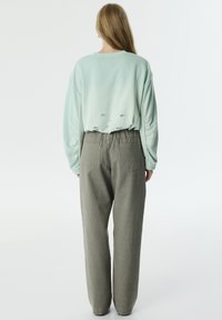 Sudadera de gran tamaño en verde menta con desgastes en la parte trasera, combinada con pantalones gris de tiro alto que tienen bolsillos traseros y un ajuste relajado.