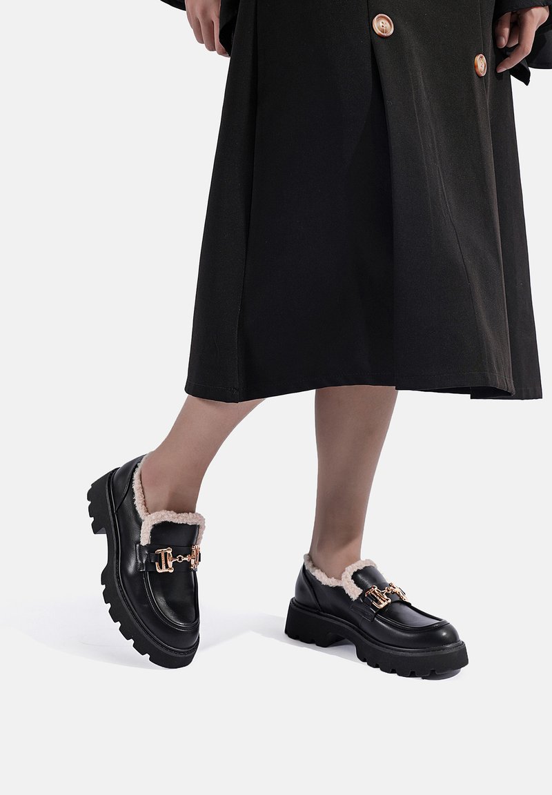 Mocassini in pelle nera con un rivestimento beige morbido, dettagli in metallo dorato e suole in gomma spesse, progettati per il comfort e la durata.