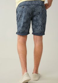 Shorts pour hommes de couleur marine avec un motif de palmiers, fabriqués en tissu léger. Dotés de poignets roulés et de deux poches arrière avec des fermetures à bouton.