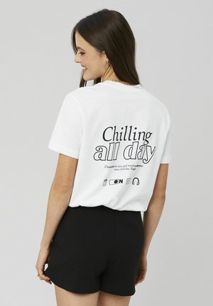 T-shirt en coton blanc avec le texte "Chilling all day" au dos dans différentes polices, accompagné de simples icônes en dessous. Manches courtes et col rond.