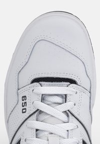 Biała sneaker z cholewką ze skóry z czarnymi akcentami, siateczkowym językiem i perforacjami. Posiada sznurowadła i gumową podeszwę. Numer modelu 650.