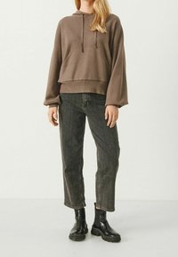 Brown pullover hoodie with a kangaroo pocket, relaxed fit, wide sleeves, paired with high-waisted black cropped jeans and black ankle boots.