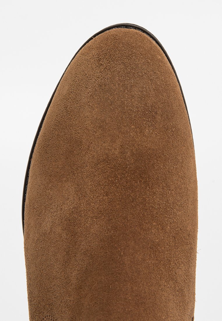 Braune Wildleder-Ankle-Boots mit glatter Textur, runder Zehenpartie und schwarzem Besatz entlang der Sohle. Keine auffälligen Muster oder Hardware-Details.