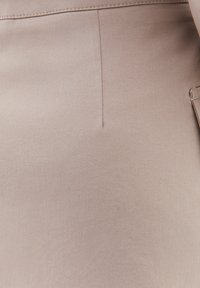 Beige stof med en glat, vævet tekstur, der har subtile syninger og en ren finish. Designet er skræddersyet og minimalistisk.