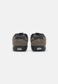 Pereche de sneakers din suede gri Vans văzuți din spate, cu tălpi negre și logo-ul "Vans Off The Wall" pe etichetele din spate.