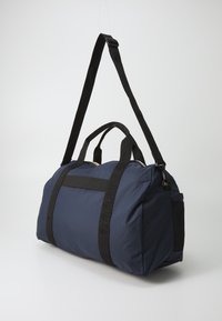 Borsa da viaggio blu navy con spallacci neri, apertura con zip, grande scomparto principale e tasca laterale in rete per ulteriore spazio di archiviazione. Materiale in nylon texturizzato.