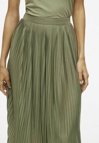 Gonna plissettata verde oliva con una fascia elastica morbida e aderente, caratterizzata da pieghe verticali uniformemente distanziate che creano una texture fluida.