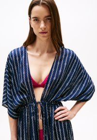 Mornarski kimono-stil prekrivač s bijelim uzorkom lanca, širokim rukavima i podesivim vezicom. Nosite ga preko ružičaste bikinijeve gornje strane.