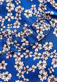 Niebieska tkanina z kwiatowym wzorem z białymi i różowymi kwiatami, czarnymi akcentami oraz falbanami wzdłuż krawędzi. Gładka tekstura.