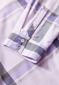 Manche de chemise à carreaux violet et gris avec deux boutons violets sur le poignet, montrant la texture du tissu et les détails de couture.