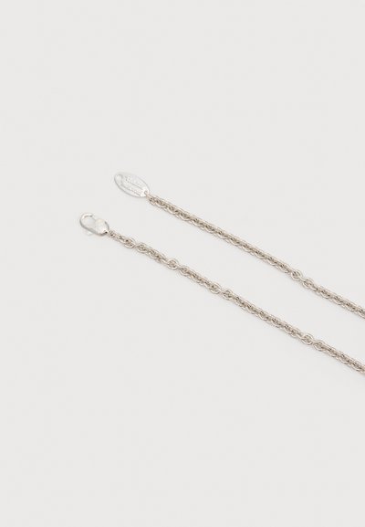 Κολιέ αλυσίδα ασημένιου τόνου με κούμπωμα λιβερπάρι και μικρή οβάλ ετικέτα με χαραγμένο κείμενο μάρκας σε ανοιχτό φόντο.