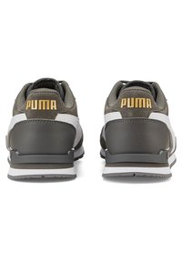 Pár šedých a bílých tenisek Puma zobrazených zezadu, s žlutým logem Puma na patě a texturovanými podrážkami.