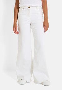 Jeans anchos blancos hechos de denim, con una cintura alta y un dobladillo deshilachado. Combinados con zapatillas blancas, tienen herrajes en tono dorado.