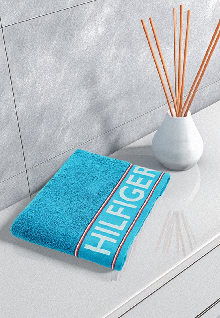 Türkises Handtuch aus flauschiger Baumwolle, mit einem weißen und roten gestreiften Rand, der das Wort "HILFIGER" in fetten, Großbuchstaben zeigt.