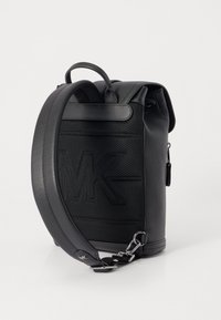 Black leather backpack with textured surface, featuring a rolled top, adjustable strap, and embossed logo detail. Silver hardware accents.