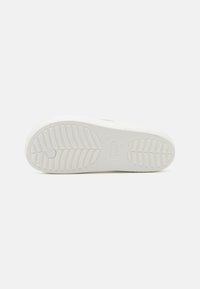 Semelle de chaussure en caoutchouc blanc avec un motif de relief texturé et un détail de logo circulaire. Fini lisse avec un point central surélevé pour une meilleure adhérence.