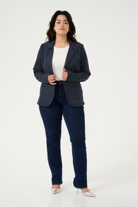 Námořnický blazer s přiléhavým střihem, vysoce kvalitní klopy, nošený přes bílý top, v kombinaci s tmavě modrými džínami a stříbrnými lodičkami s špičatou špičkou.