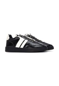 Zapatillas negras con un acabado de charol texturizado, rayas diagonales blancas y suelas de goma negra. Los cordones están asegurados con ojales metálicos.