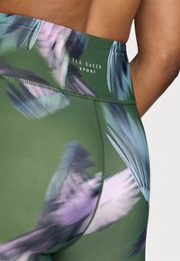 High-waisted athletic leggings in green with a multicolored feather pattern. Features logo print and seamless stitching for comfort.