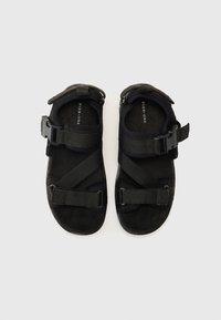 Black sandals with adjustable fabric straps and a sturdy buckle. The sole is flat with a textured finish and cushioned interior.
