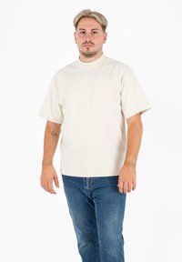 Crème t-shirt met korte mouwen, voorzien van getextureerde horizontale naden, ronde hals en een losse pasvorm, gecombineerd met blauwe jeans met een vervaagde afwerking.