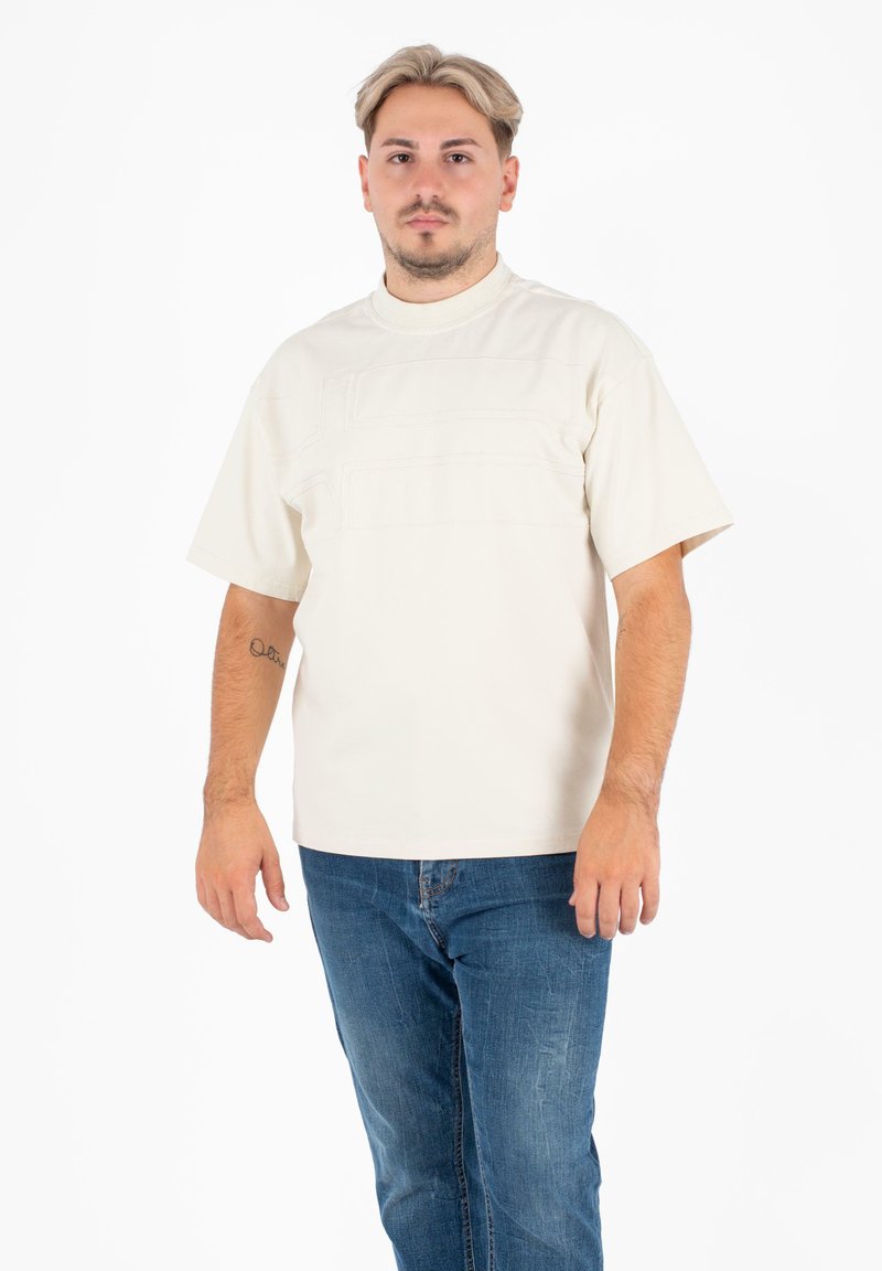 Crème t-shirt met korte mouwen, voorzien van getextureerde horizontale naden, ronde hals en een losse pasvorm, gecombineerd met blauwe jeans met een vervaagde afwerking.
